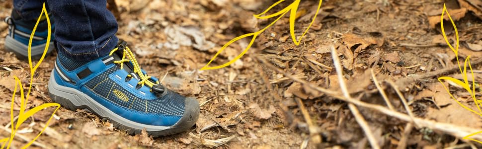 a child stands on brown leaves and twigs in the dirt wearing a dark and light blue chandler sneaker