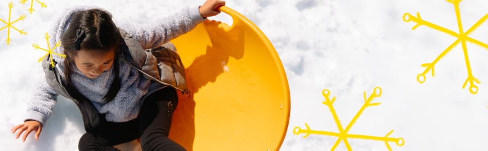 A young girl sits sideways on an orange sled in the snow wearing a fuzzy sweater under a vest.